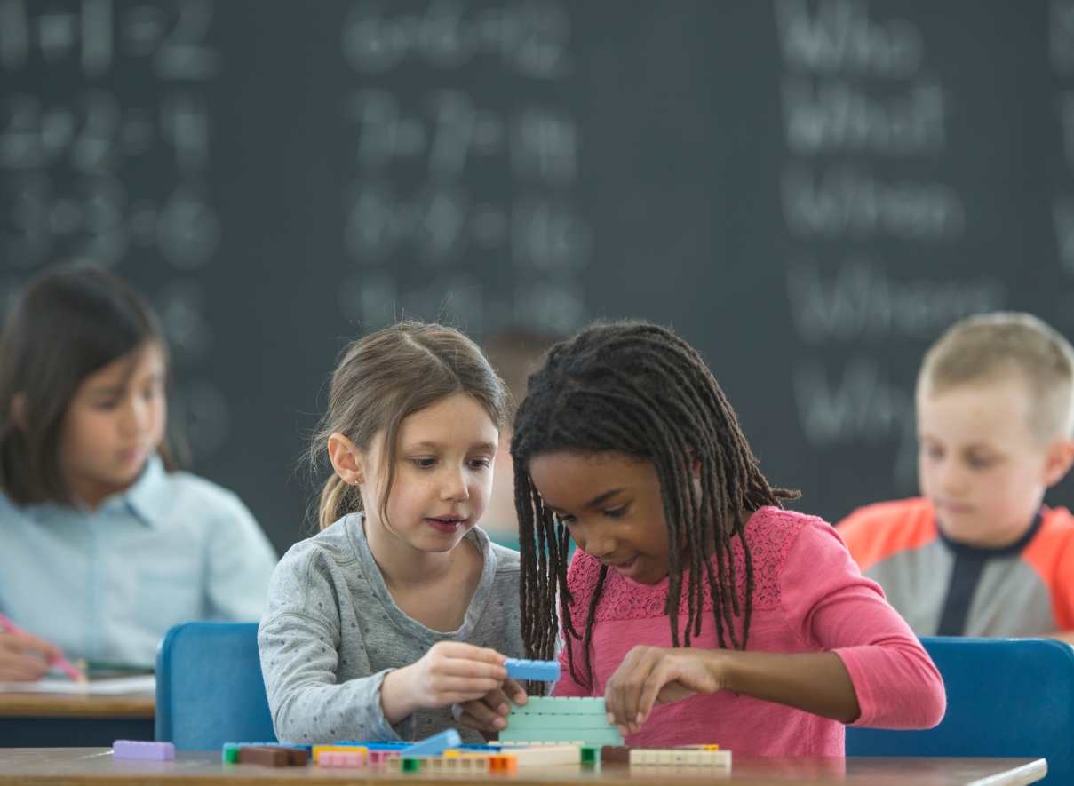 Two elementary school girls in a math classroom playing with building blocks on a table. 